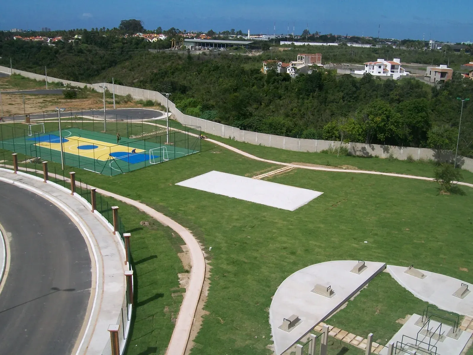 Área de lazer vista de cima, com a quadra poliesportiva pintada em azul e amarelo e a praça circular