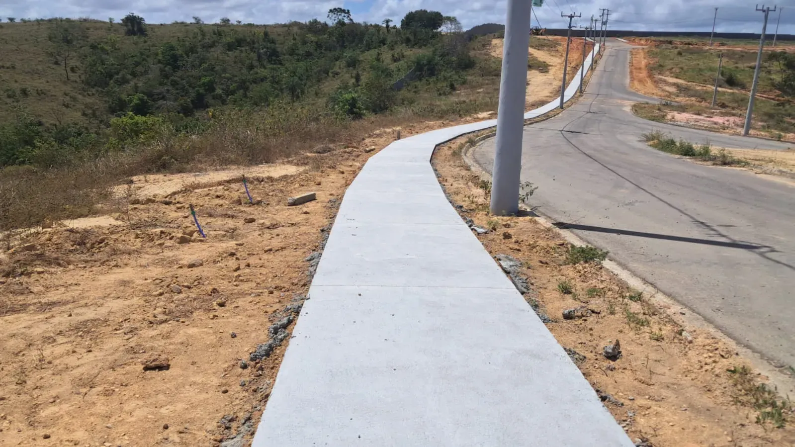 Trecho de calçada já concretado ao longo da via, entre o talude e a rua.