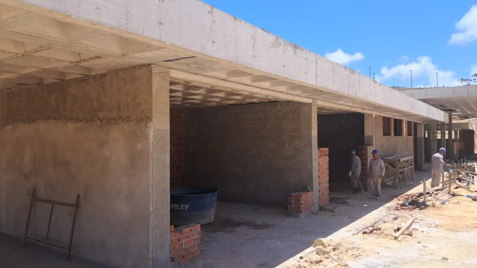 Paredes de alvenaria sob a laje nervurada, com a equipe trabalhando ao fundo.