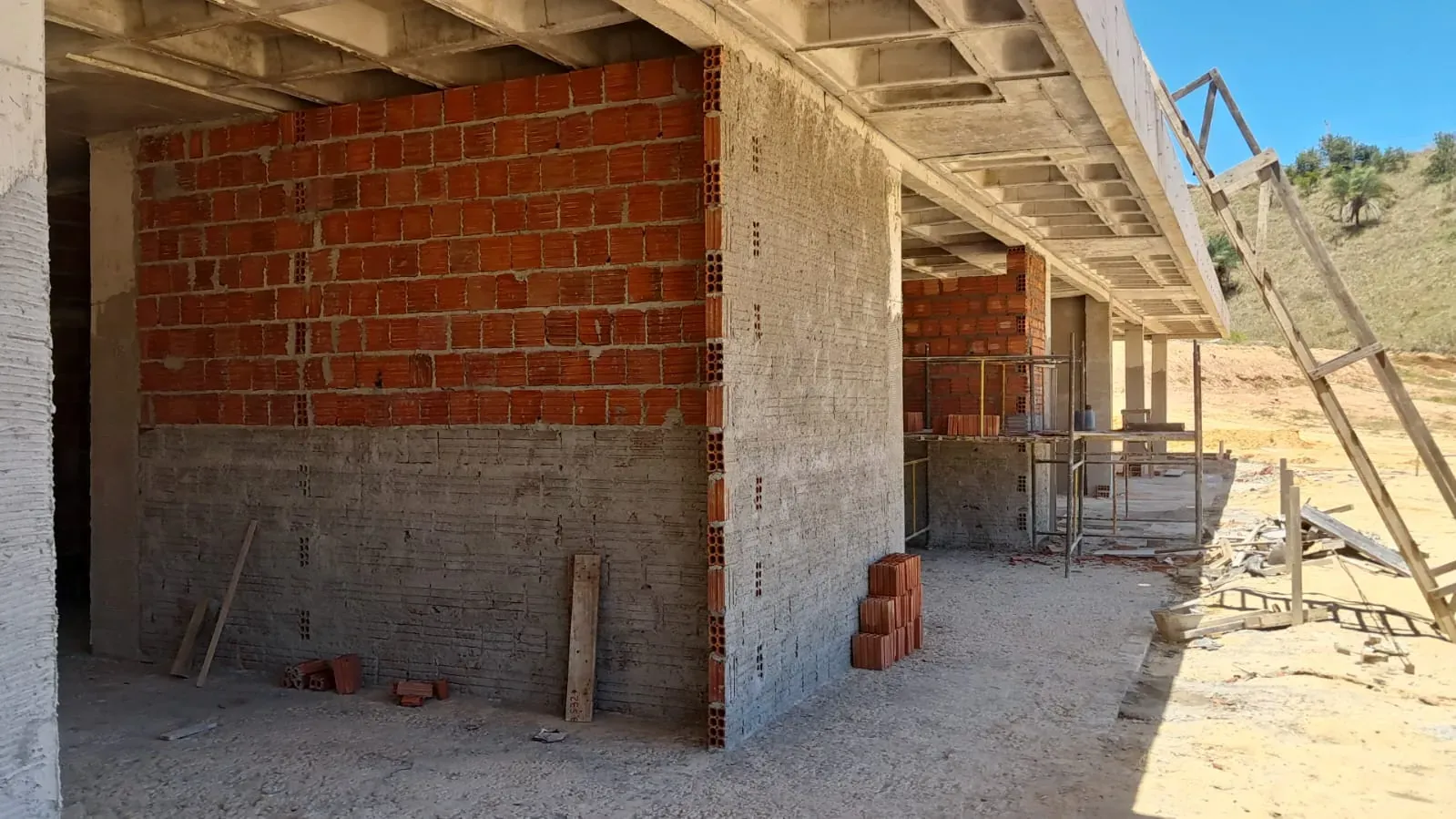 Parede de tijolo cerâmico erguida até a laje, com o andaime montado ao fundo.