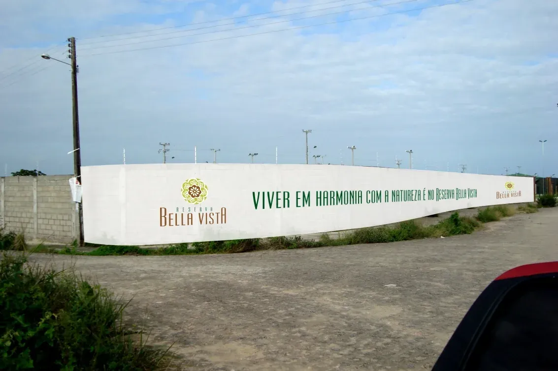 Muro do Reserva Bella Vista pintado de branco, com o logotipo e a frase "Viver em harmonia com a natureza é no Reserva Bella Vista"