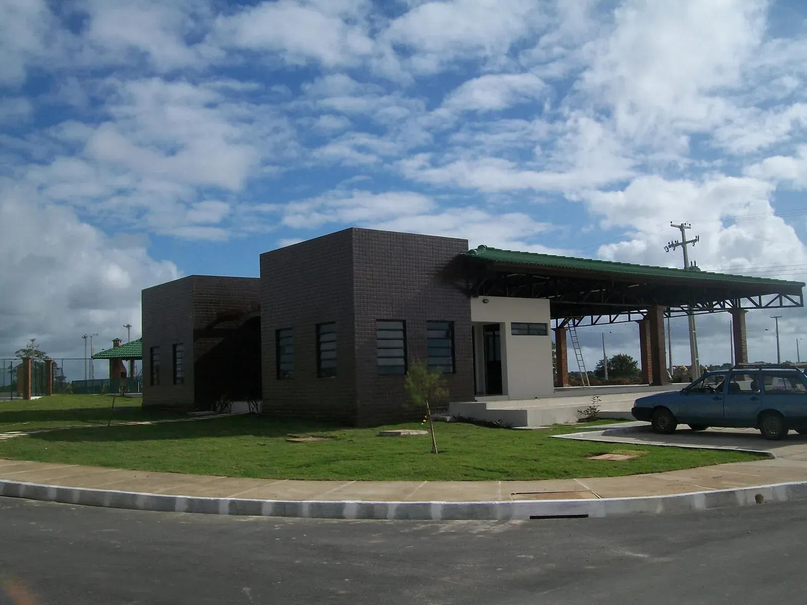 Prédio da portaria em tijolo escuro com telhado verde e a guarita ao lado